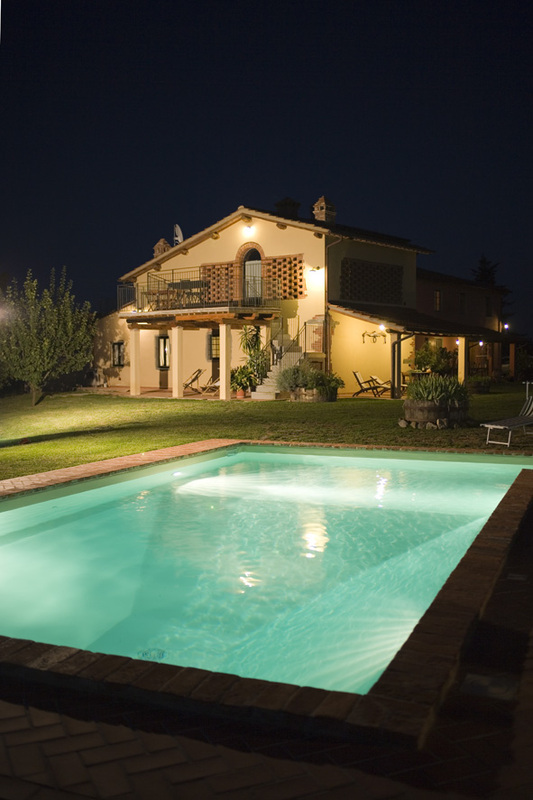 La piscina illuminata di sera, con il casale sullo sfondo
